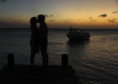 senior couple kissing at sunset with a boat and ocean in the backgroundの写真素材