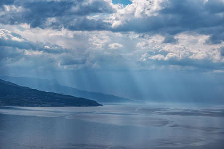 Distant sea shores under the sun rays through the cloudsの写真素材