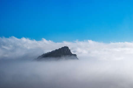 The top of the mountain with a geodesic sign rises above the fog with blue sky backgroundの写真素材