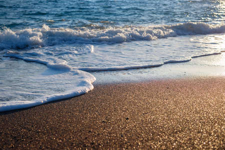 Sea surf on a sandy beach at sunset selective focusの写真素材