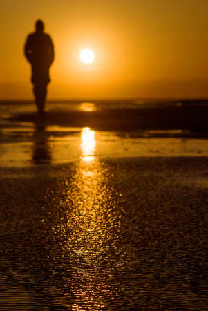 Sunset with reflection and blurred silhouette of a lonely man in the backgroundの写真素材
