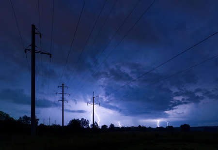 Silhouette of power lines on thunderstorm with lightnings backgroundの写真素材