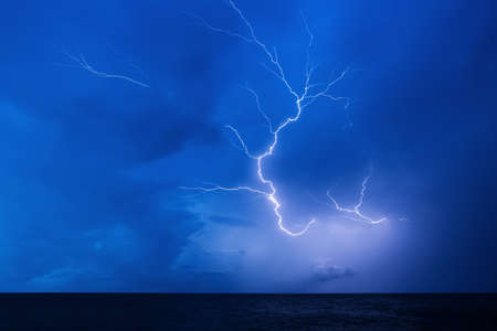 Powerful lightning in the blue sky over the dark seaの写真素材
