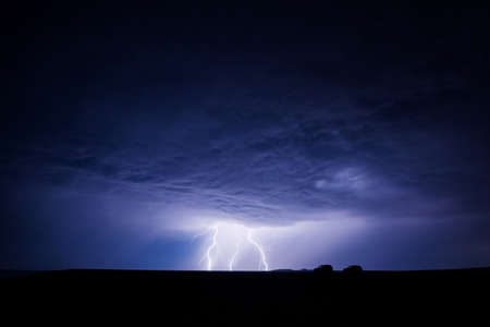 Lightning over the plain with silhouettes of two cars in the foregroundの写真素材