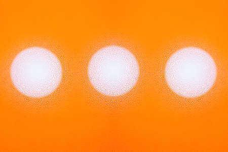 Abstract texture of multiple water drops on glass with an orange background with three white circlesの写真素材