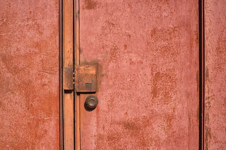 A fragment of a rusty red metal door with a closed lock and a round handleの写真素材