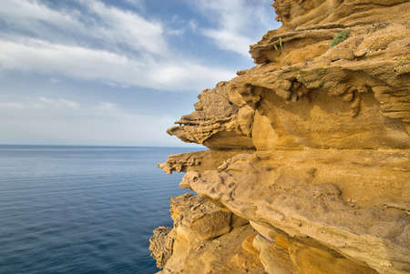 Weathered sandstone on the sea and sky with clouds backgroundの写真素材