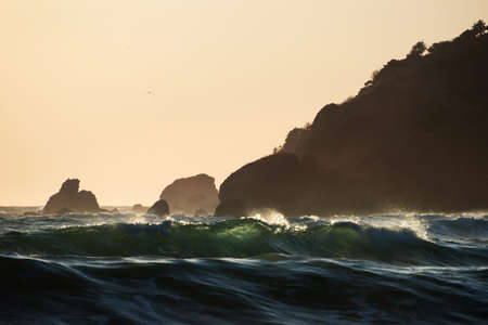 Green sea waves at sunset in front of the stone capeの写真素材