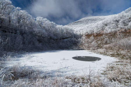 A small frozen pond in the frosty forest under the mountainの写真素材