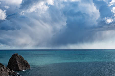 Dramatic rain clouds over the Black sea with a coastal rock in the foregroundの写真素材