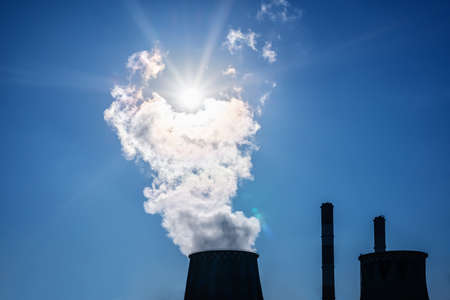 Silhouette of CHP pipes with steam on a blue sky with a radiant sun backgroundの写真素材