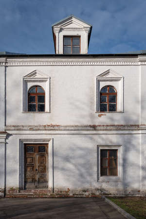 Fragment of the facade of an old 18th century building in traditional russian style with windows and a wooden door with a padlockの写真素材