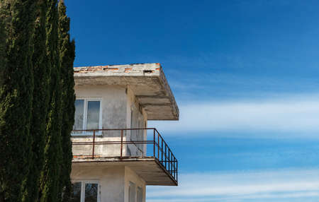 A white shabby modern house with cypress trees in the foreground and a blue sky with beautiful clouds in the backgroundの写真素材