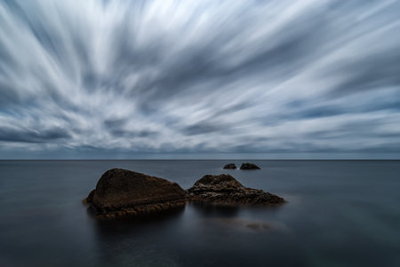 Minimalistic long exposure night seascape with motionless water, four rocks and moving cloudsの写真素材
