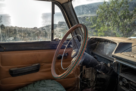 The interior of an old abandoned car with cobwebs, spiders and a thick layer of dust, selective focus on the steering wheel braided with colored wiresの写真素材