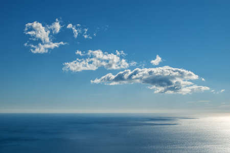 Light white clouds on a sunny day over a calm sea with reflection