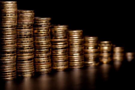 Descending stacks of brass coins with reflection and selective focus on a black backgroundの写真素材