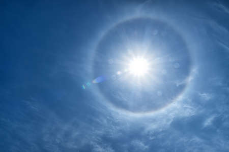 A halo around a radiant sun with lens flare in a blue sky.の写真素材