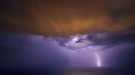 A night thunderstorm over the sea with multicolored clouds.の写真素材