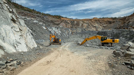 Heavy machinery (excavator, hydraulic hammer) in an open pit stone quarry.の写真素材
