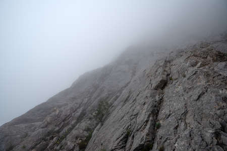 Steep rock cliffs disappearing into the fog, view from below.の写真素材