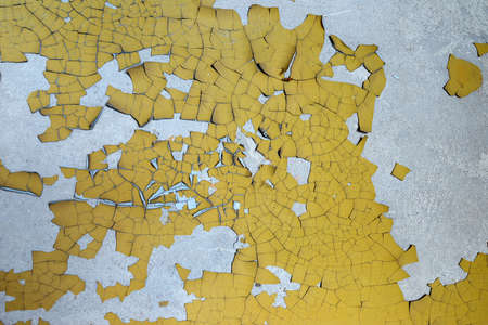The texture of cracked, peeling yellow paint on a gray concrete wall.の写真素材