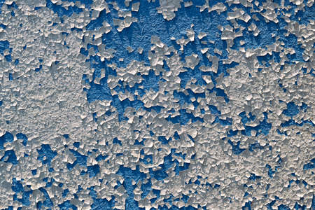 A full-screen texture of cracked, partially exfoliated white paint on a blue wall.の写真素材