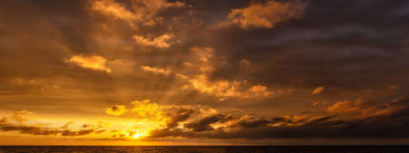 Dramatic golden sunset with sun rays over the sea, horizontally panoramic.の写真素材
