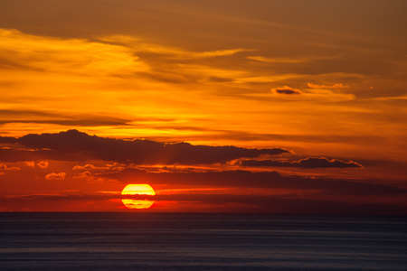 The orange setting sun in the clouds over the dark sea.の写真素材