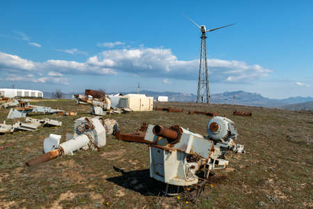 An abandoned wind power station with one wind turbine and rusty spare parts in the foreground.の写真素材