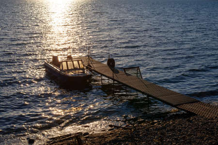 An old battered motor boat near a small rusty metal pier at sunset.の写真素材