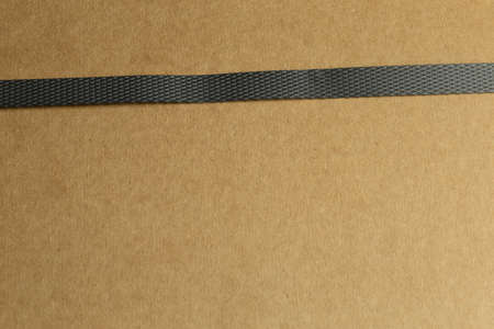 Package of brown cardboard with slightly slanted single dark gray parcel tape photographed in oblique close-up with bokeh in background and foregroundの写真素材
