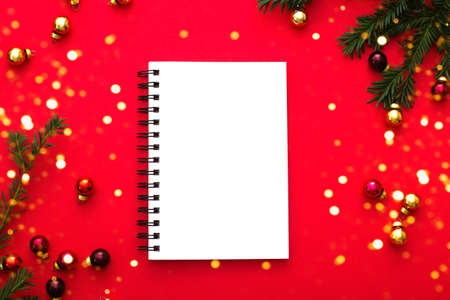 Notebook white mockup on red background with golden christmas decorations, green fir tree brunch, blurred golden festive lights. Christmas time concept. Flatlay styleの写真素材