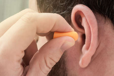 Man putting ear plugs into ears to protect hearing and get rid of noise. Concept for World Hearing Day campaignの写真素材