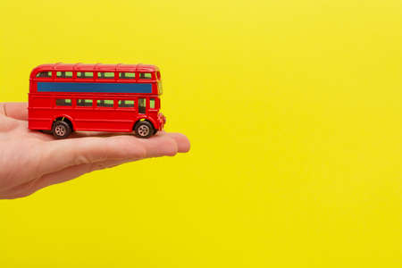 British toy double-decker red bus holding by male hand on yellow background with copy space for your text. Concept of English language lessonの写真素材