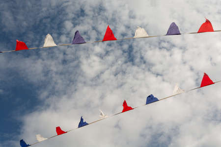 Multicolor pennant banner, triangle festival flags, decoration for outdoor event, open air party, backyard picnic. Decorative flags with cloudy sky on backgroundの写真素材