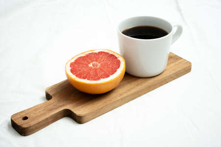 Grapefruit and big mug of black Americano coffee on wooden board for a diet meal plan breakfastの写真素材