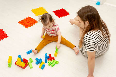 Mother teaching her little child daughter to build with constructor colorful block sitting on the...