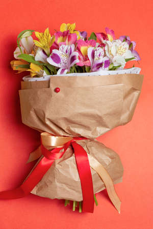 Aesthetic bouquet with multicolor alstroemeria flower in craft paper with red pin decoration on red background. Woman international day or romantic date conceptの写真素材