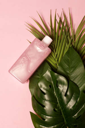 Top view of mockup of cosmetic battle with nacre textured liquid in pink color with tropical leaves.