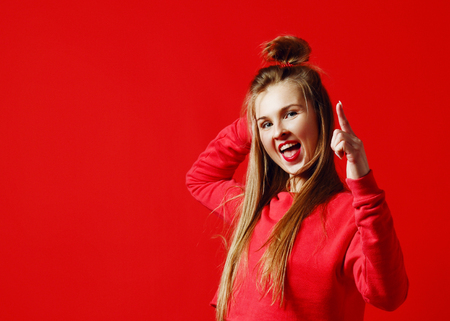 Pretty young female has long light hair, pleasant smile, makes gesture with index finger, isolated over red background, copy space for advertismentの写真素材