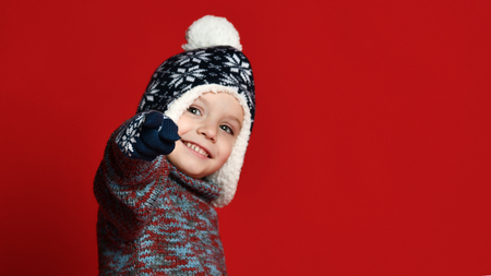 Portrait of a little cute boy wearing a knitted hat, sweater and gloves mittens, shows an alt to the...