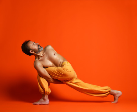 Studio shot of senior bearded man doing yoga poses and stretching his legs shirtlessの写真素材