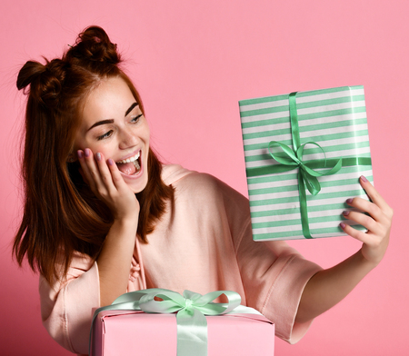 Portrait of a pretty smiling redhead girl woman holding small gift box with ribbon. Soft colors. Studio portrait over pink background,の写真素材