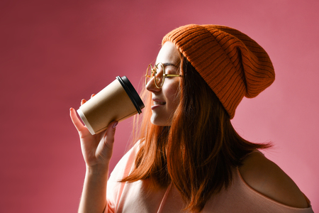 Close-up side photo of pretty red head woman in warm clothes drinking hot tea, isolated on pink backgroundの写真素材