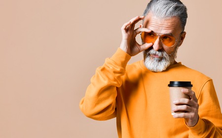 handsome bearded man in a yellow sweatshirt and trendy yellow glasses with paper cup of morning coffeeの写真素材