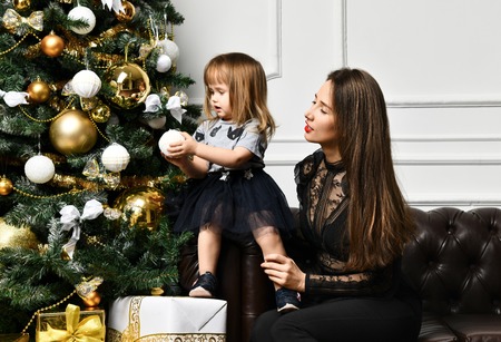 Mother with her child daughter dressed black suit in beautiful fashion celebrating near , Decorating the Christmas treeの写真素材