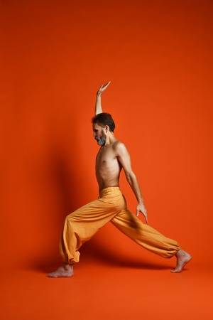 Old man practicing yoga doing stretching exercises against orange backgroundの写真素材