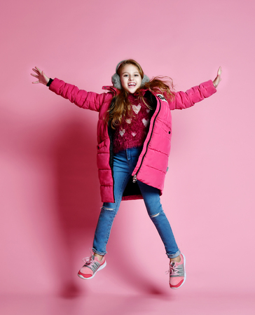 Young fashion child girl jumping over pink background, she dressed in short violet down jacket and jeans. fashion kidsの写真素材
