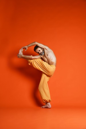 Old man practicing yoga doing stretching exercises against orange backgroundの写真素材